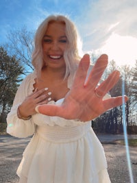 a woman in a white dress is holding up her hand